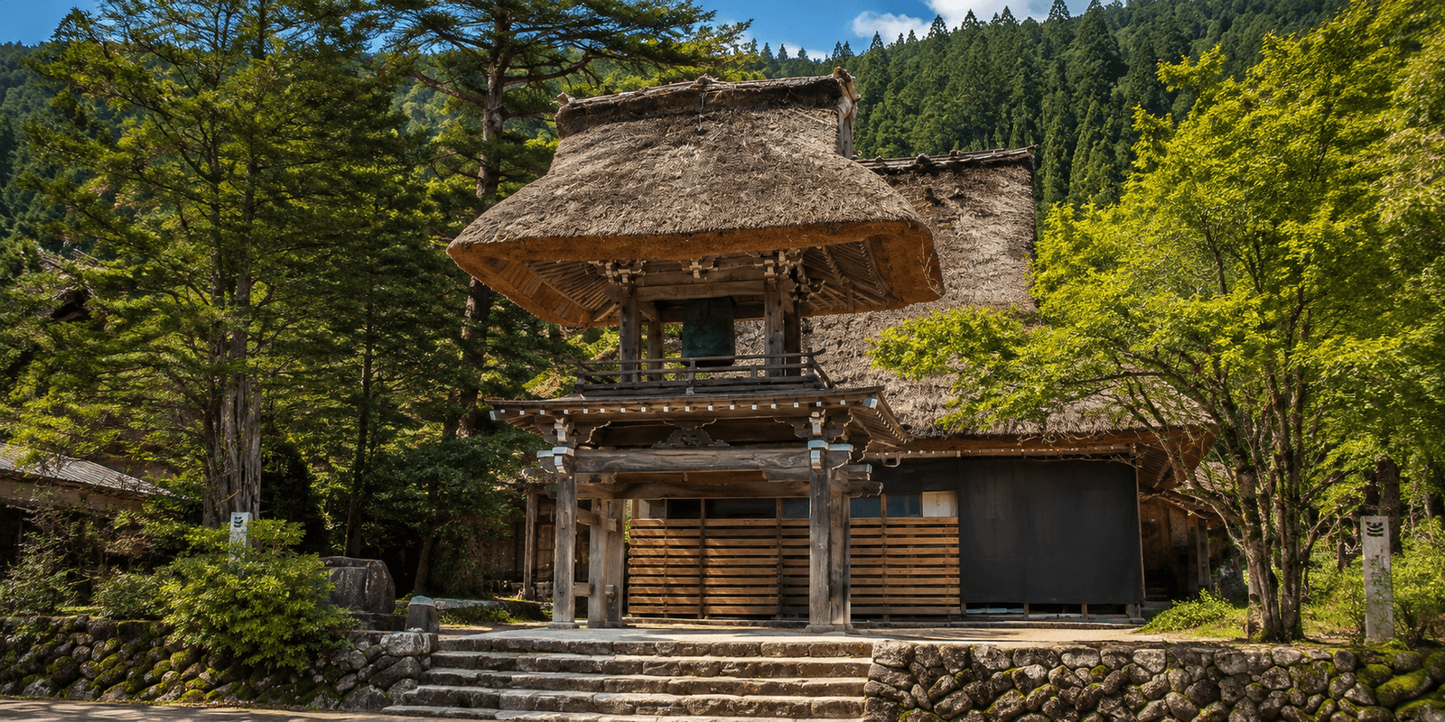 The thatched hip roof of Myozenji's Shoromon bell tower gate set against a forested hillside in Ogimachi, Shirakawa-go